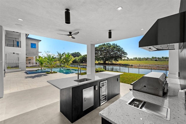 view of patio / terrace with wine cooler, area for grilling, sink, a water view, and a fenced in pool