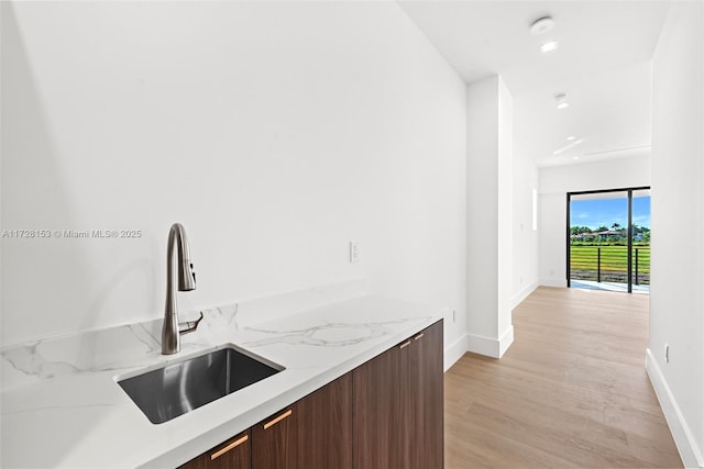 interior space with light stone countertops, sink, light hardwood / wood-style floors, and dark brown cabinetry