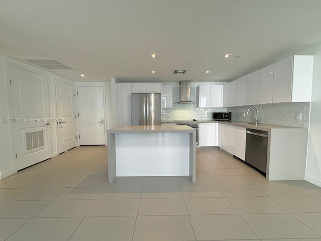 kitchen with white cabinetry, appliances with stainless steel finishes, decorative backsplash, wall chimney exhaust hood, and a center island