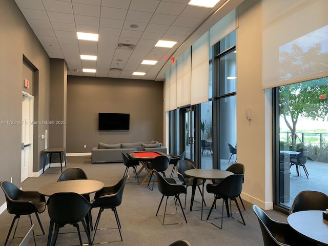 carpeted dining area featuring a drop ceiling and a towering ceiling