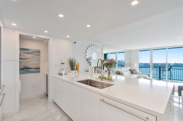 kitchen featuring floor to ceiling windows, sink, an island with sink, a water view, and white cabinets