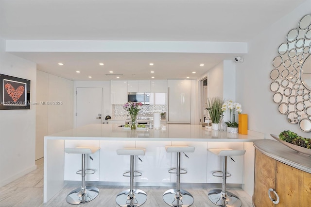 kitchen with kitchen peninsula, white cabinets, a breakfast bar, and decorative backsplash