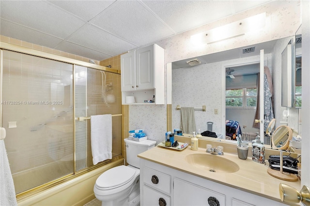 full bathroom featuring shower / bath combination with glass door, a paneled ceiling, vanity, toilet, and ceiling fan