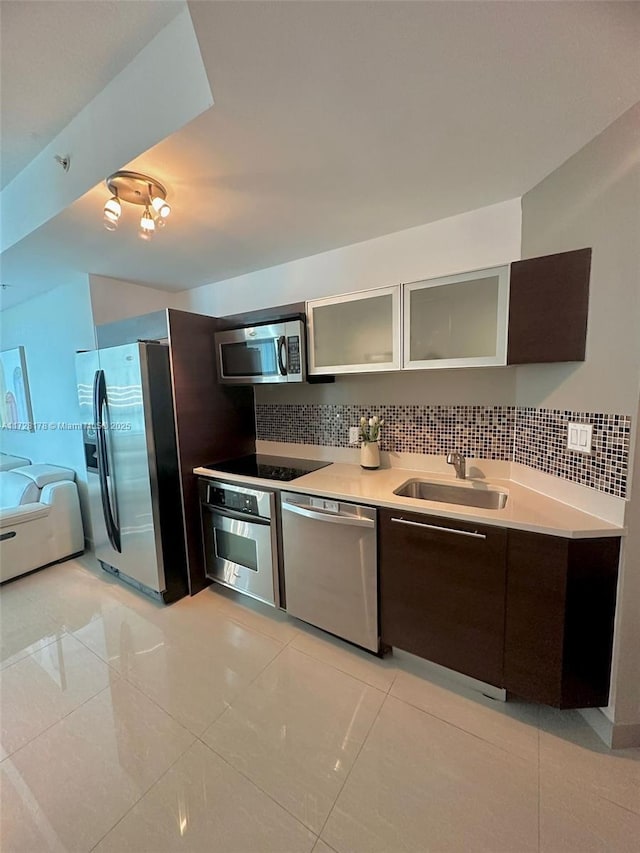 kitchen with a sink, tasteful backsplash, stainless steel appliances, light countertops, and glass insert cabinets