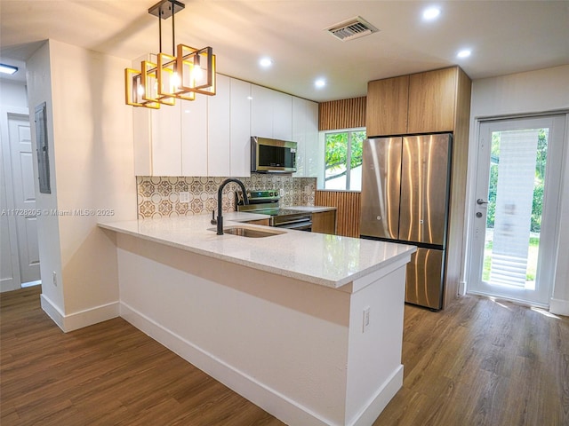 kitchen with light stone countertops, white cabinets, appliances with stainless steel finishes, sink, and hanging light fixtures