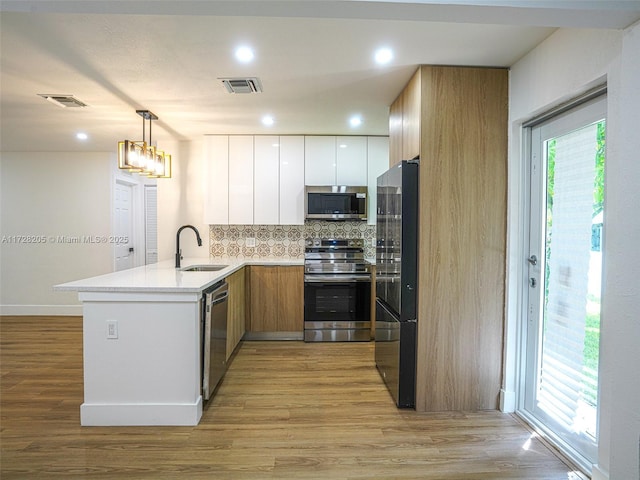 kitchen with decorative light fixtures, kitchen peninsula, sink, white cabinetry, and appliances with stainless steel finishes