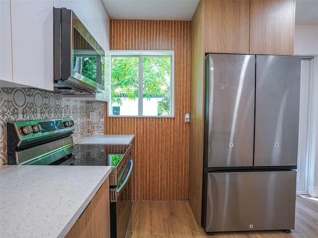 kitchen featuring light hardwood / wood-style floors, decorative backsplash, white cabinetry, stainless steel appliances, and light stone counters