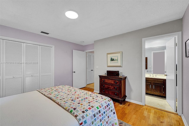 bedroom featuring light hardwood / wood-style floors, connected bathroom, a closet, a textured ceiling, and sink