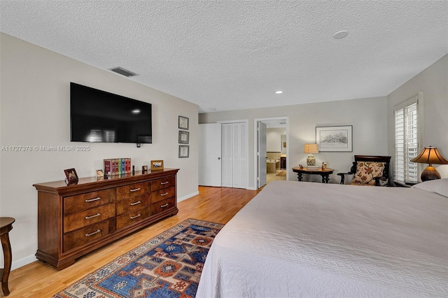 bedroom with ensuite bath, light wood-type flooring, and a textured ceiling