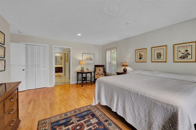 bedroom featuring a textured ceiling, a closet, light hardwood / wood-style flooring, and ensuite bath