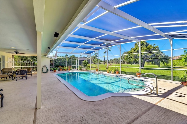 view of swimming pool with ceiling fan, glass enclosure, a lawn, and a patio