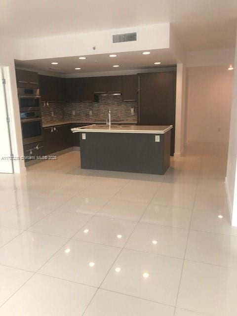 kitchen featuring a center island with sink, tasteful backsplash, light tile patterned flooring, double oven, and sink