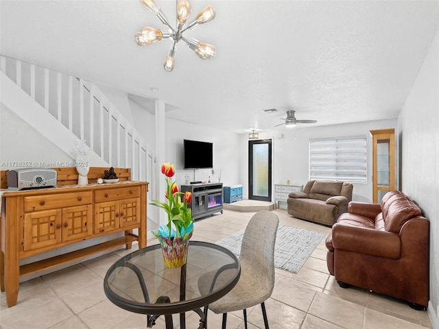 living room featuring light tile patterned floors, ceiling fan with notable chandelier, and a textured ceiling