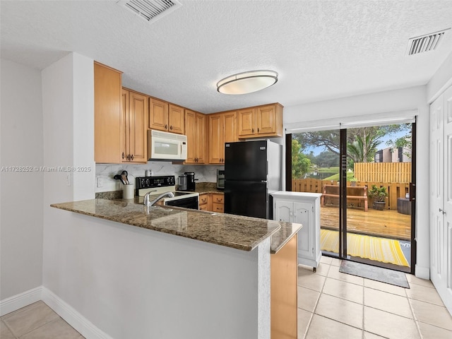 kitchen featuring light tile patterned floors, dark stone countertops, kitchen peninsula, and black refrigerator