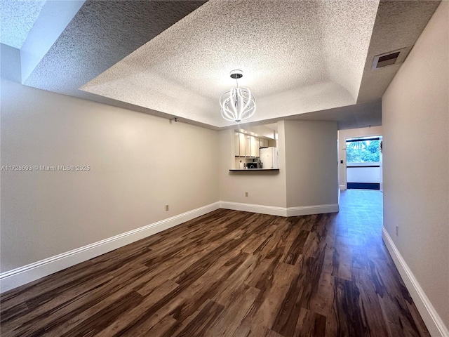 unfurnished dining area featuring a notable chandelier, dark hardwood / wood-style floors, a raised ceiling, and a textured ceiling