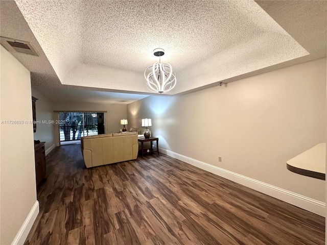 unfurnished living room with an inviting chandelier, a tray ceiling, dark hardwood / wood-style flooring, and a textured ceiling