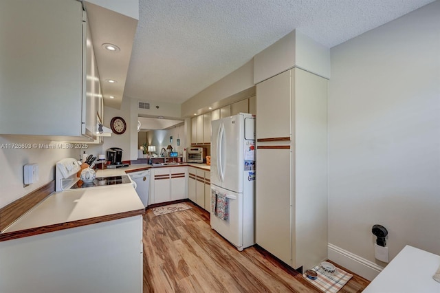 kitchen with sink, white appliances, light hardwood / wood-style floors, and kitchen peninsula