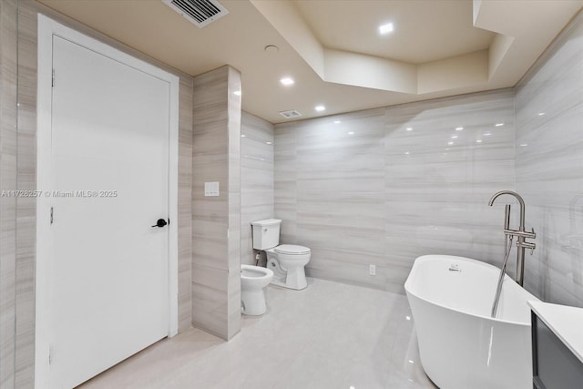 bathroom with toilet, tile walls, a bidet, and a bathing tub