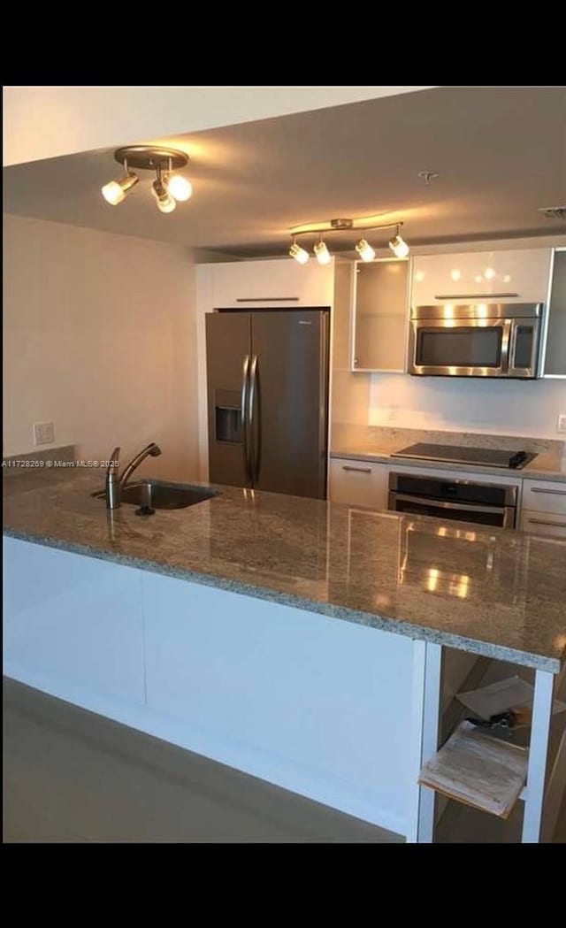 kitchen featuring kitchen peninsula, stainless steel appliances, dark stone counters, white cabinets, and sink