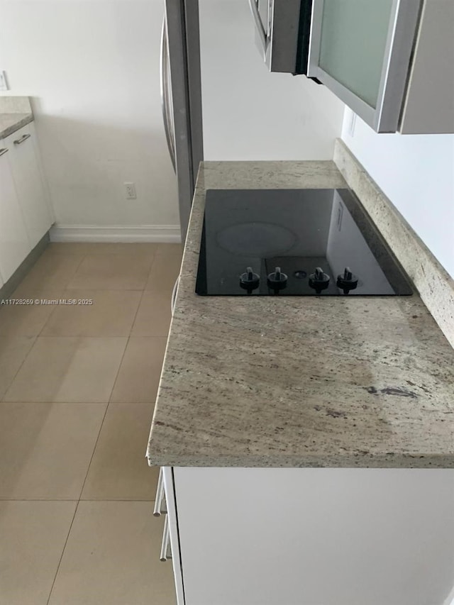 kitchen with white cabinets, light tile patterned floors, black electric stovetop, and stainless steel refrigerator