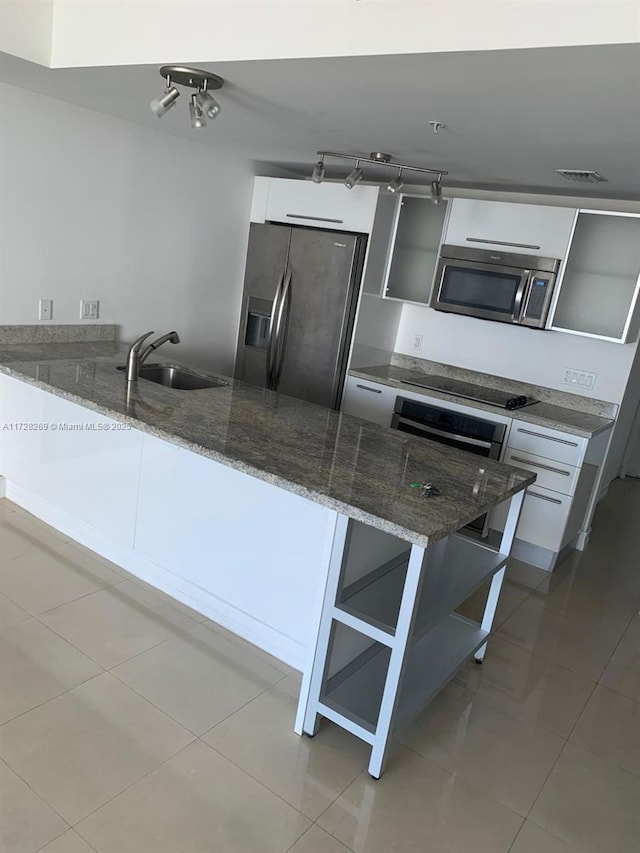 kitchen with white cabinets, appliances with stainless steel finishes, dark stone counters, sink, and kitchen peninsula