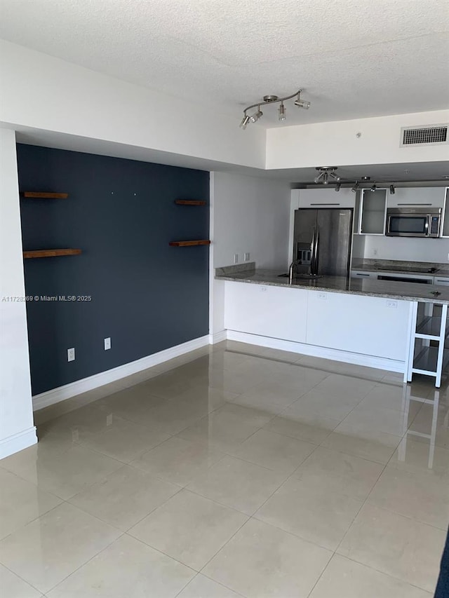 kitchen featuring track lighting, a textured ceiling, light tile patterned floors, and stainless steel appliances