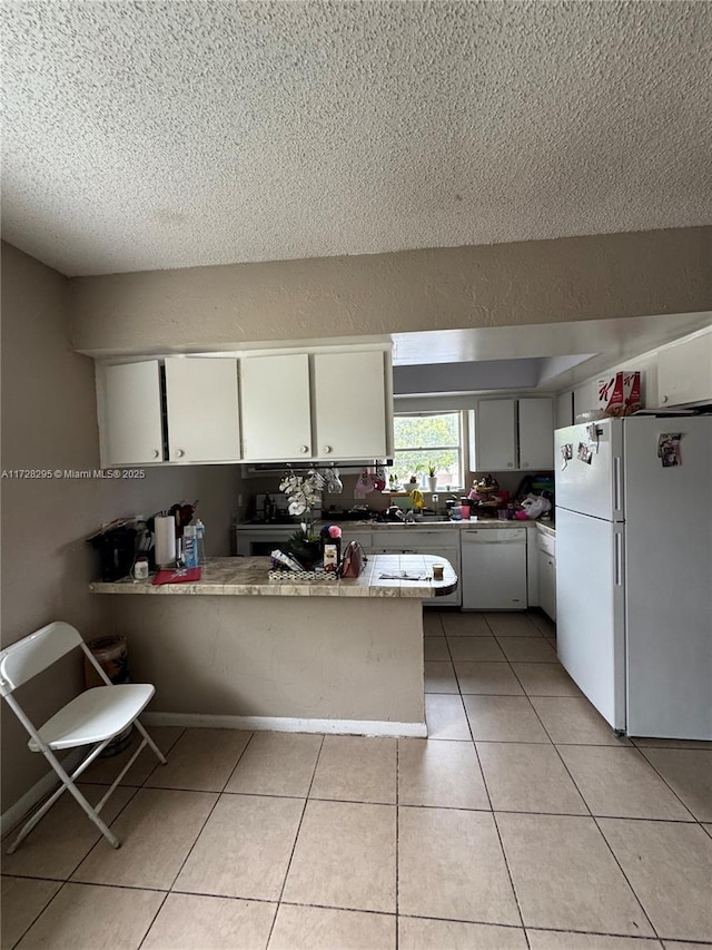 kitchen with light tile patterned floors, white cabinets, kitchen peninsula, and white appliances