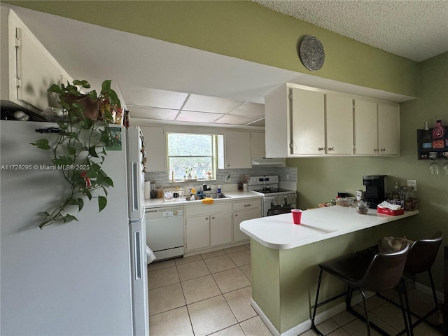 kitchen with white appliances, white cabinetry, sink, kitchen peninsula, and light tile patterned floors