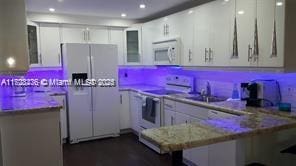 kitchen featuring white appliances, light stone countertops, white cabinets, sink, and kitchen peninsula