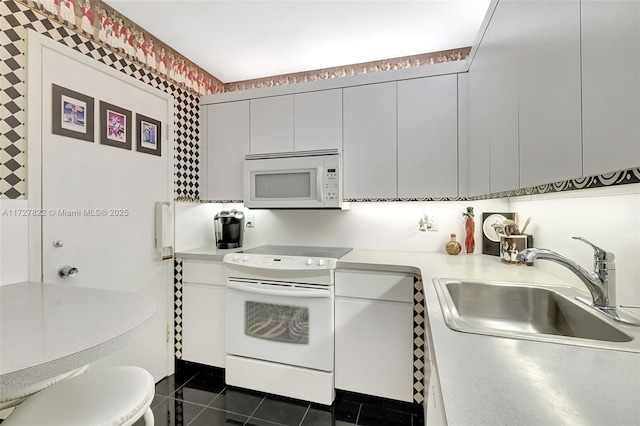 kitchen with light countertops, a sink, modern cabinets, dark tile patterned flooring, and white appliances