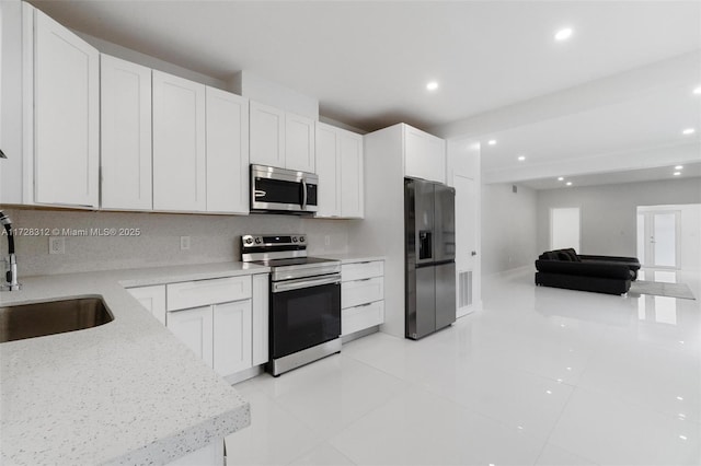 kitchen with light stone countertops, appliances with stainless steel finishes, white cabinetry, tasteful backsplash, and sink