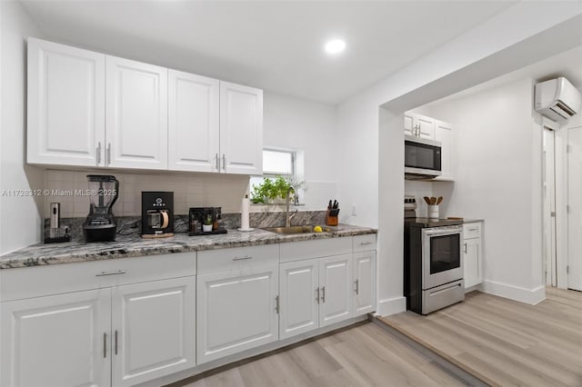 kitchen with appliances with stainless steel finishes, sink, white cabinetry, and a wall mounted air conditioner