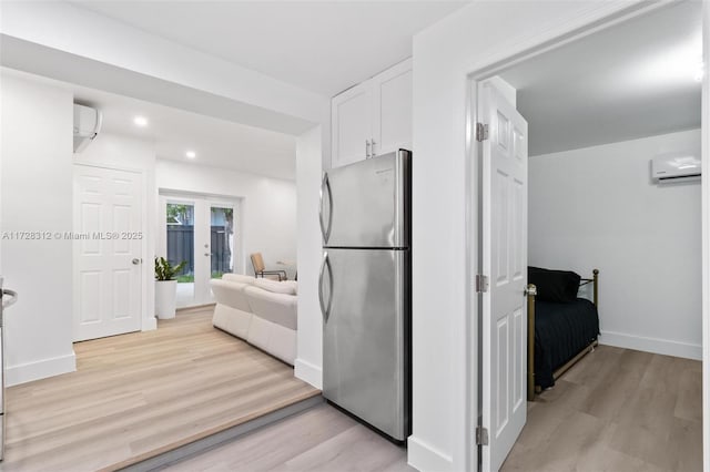 kitchen featuring a wall mounted AC, light hardwood / wood-style floors, french doors, stainless steel refrigerator, and white cabinets