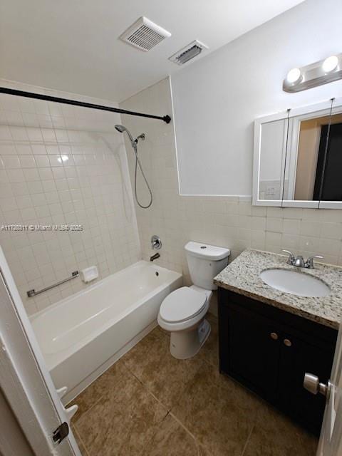 full bathroom with tiled shower / bath combo, tile patterned flooring, vanity, tile walls, and toilet