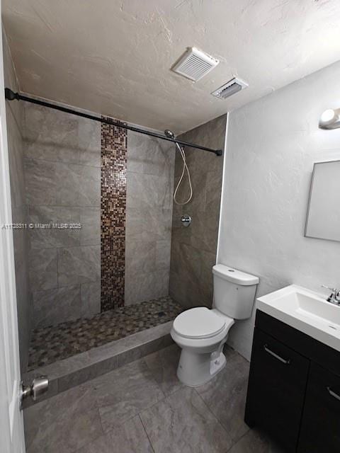 bathroom featuring toilet, vanity, and a tile shower