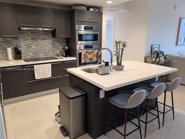 kitchen featuring tasteful backsplash, cooktop, a breakfast bar, and an island with sink