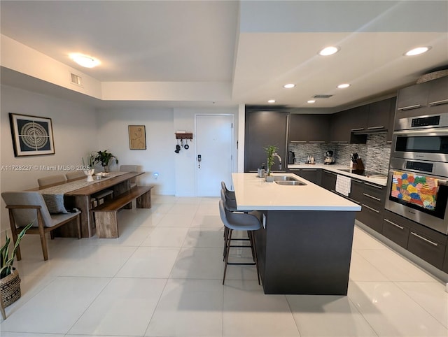 kitchen featuring a breakfast bar, a sink, light countertops, black electric stovetop, and modern cabinets