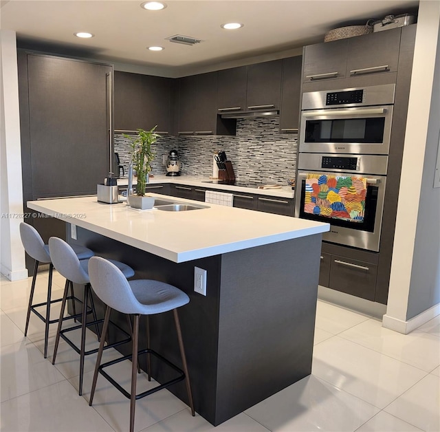 kitchen featuring a breakfast bar, light tile patterned floors, double oven, an island with sink, and decorative backsplash