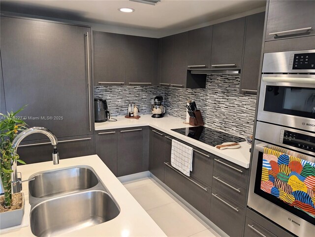 kitchen featuring sink, a breakfast bar area, a center island with sink, black electric cooktop, and stainless steel double oven