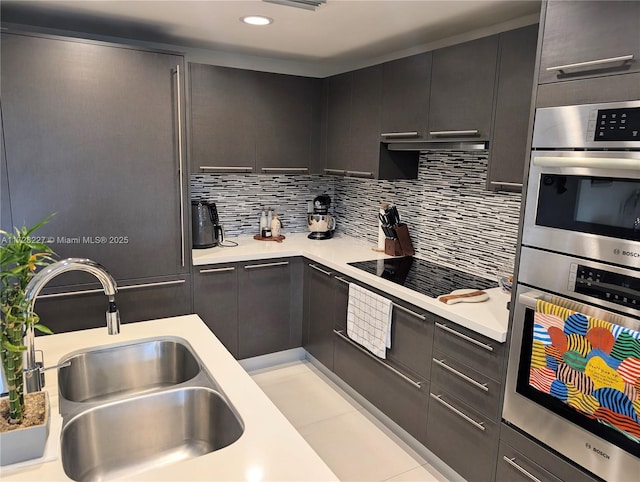 kitchen featuring a sink, backsplash, double oven, light countertops, and black electric stovetop