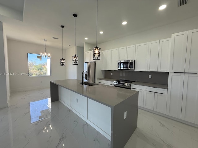 kitchen with white cabinetry, stainless steel appliances, decorative light fixtures, and a center island with sink