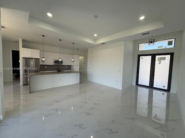 kitchen featuring hanging light fixtures, appliances with stainless steel finishes, white cabinets, and a tray ceiling