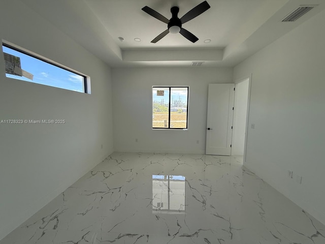 spare room with ceiling fan, plenty of natural light, and a tray ceiling