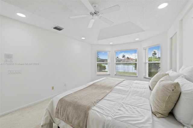 carpeted bedroom featuring a water view, ceiling fan, a tray ceiling, and a textured ceiling