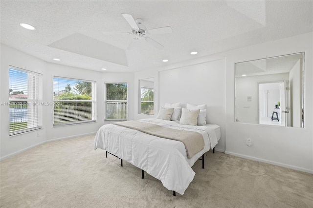 bedroom with ceiling fan, light colored carpet, and a tray ceiling