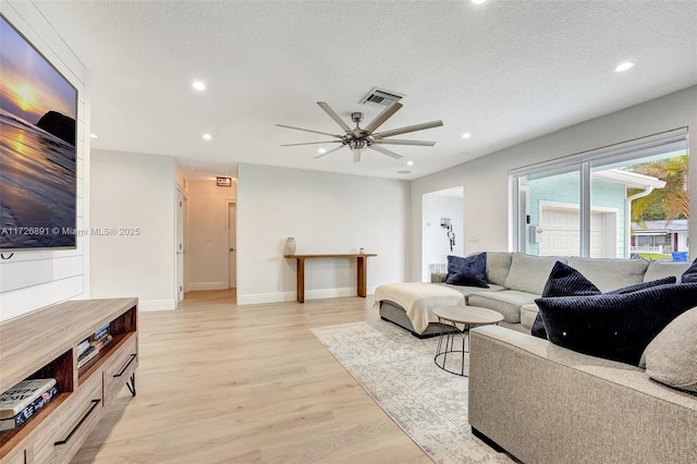 living room with a textured ceiling, ceiling fan, and light wood-type flooring