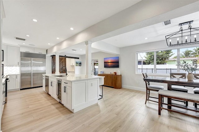 kitchen featuring a barn door, a center island with sink, sink, stainless steel appliances, and white cabinets