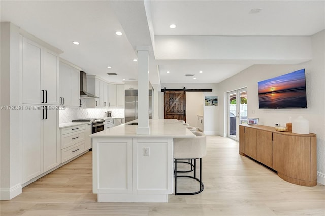 kitchen featuring white cabinets, appliances with stainless steel finishes, a kitchen island, wall chimney range hood, and a barn door