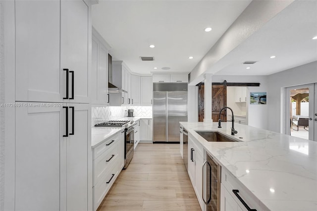 kitchen with light stone countertops, appliances with stainless steel finishes, wall chimney range hood, sink, and a barn door