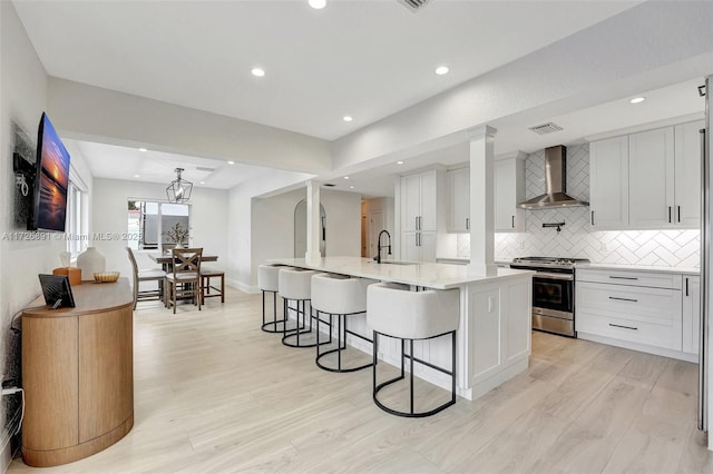 kitchen featuring stainless steel range, white cabinetry, a center island with sink, and wall chimney exhaust hood